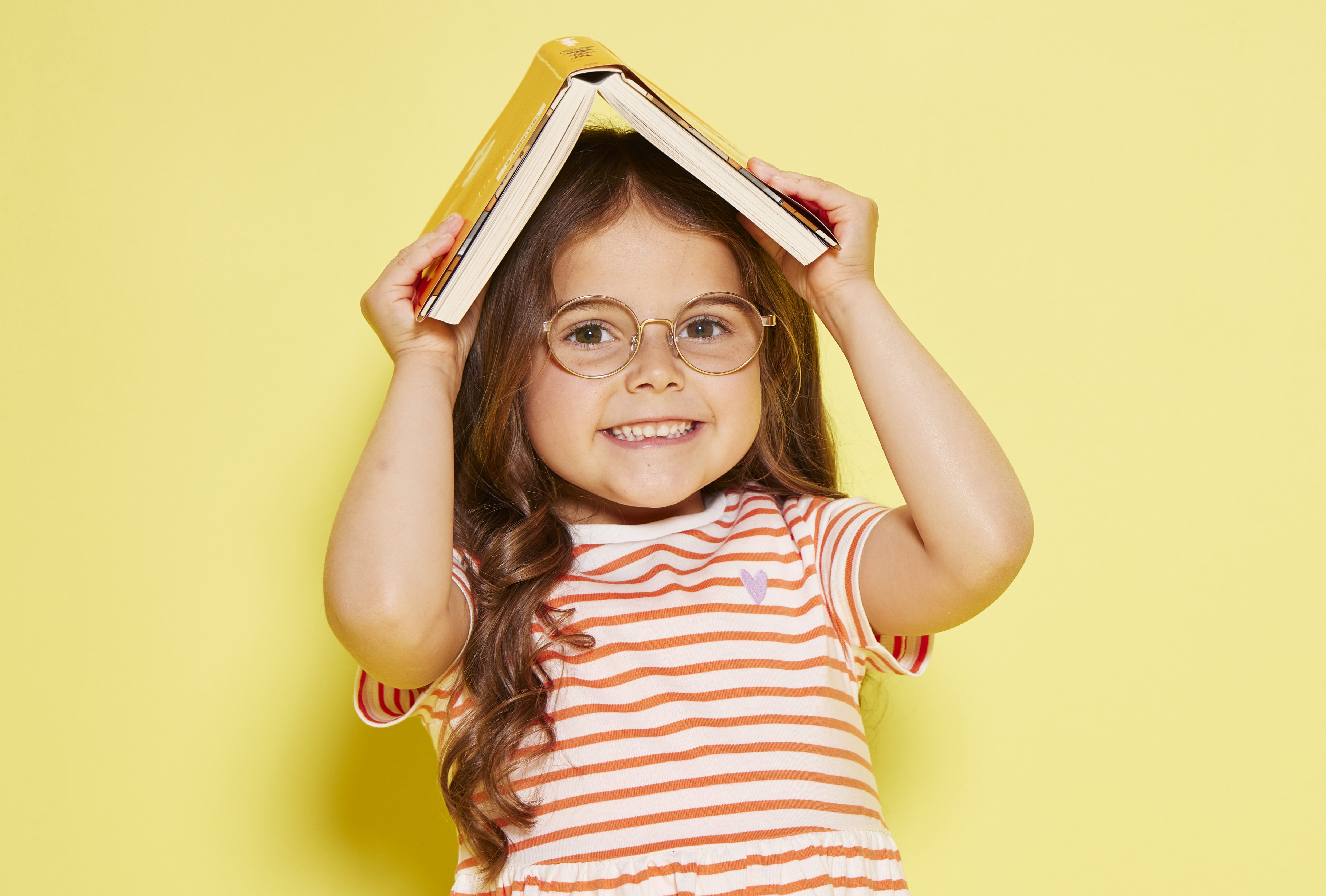 Girl holding open book on her hand with a yellow background.